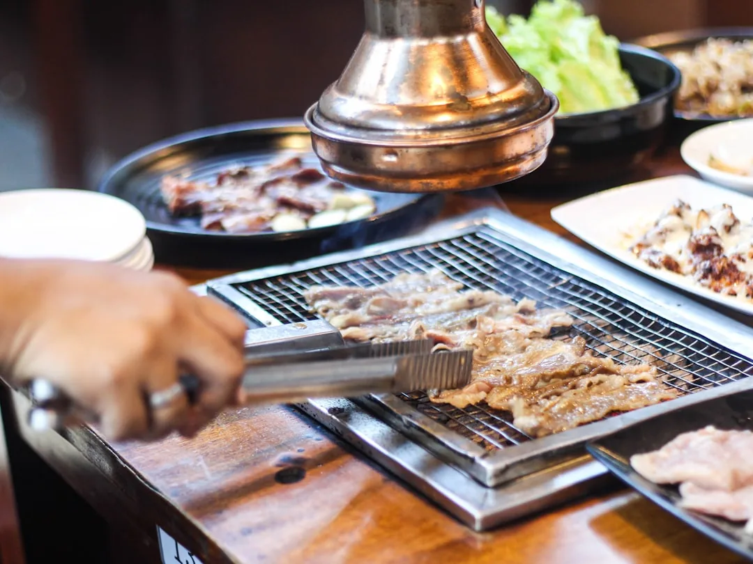 Person grilling samgyeopsal pork belly on a Korean BBQ grill