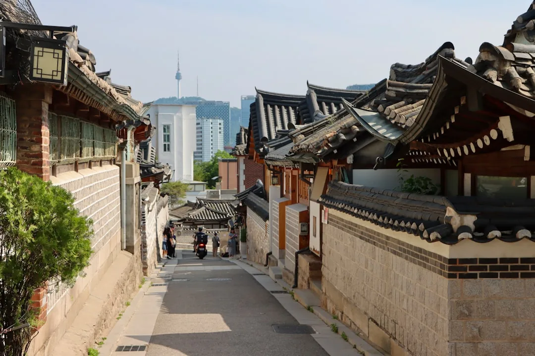 Hanok-lined street in a traditional Korean craft town, modern skyline visible beyond