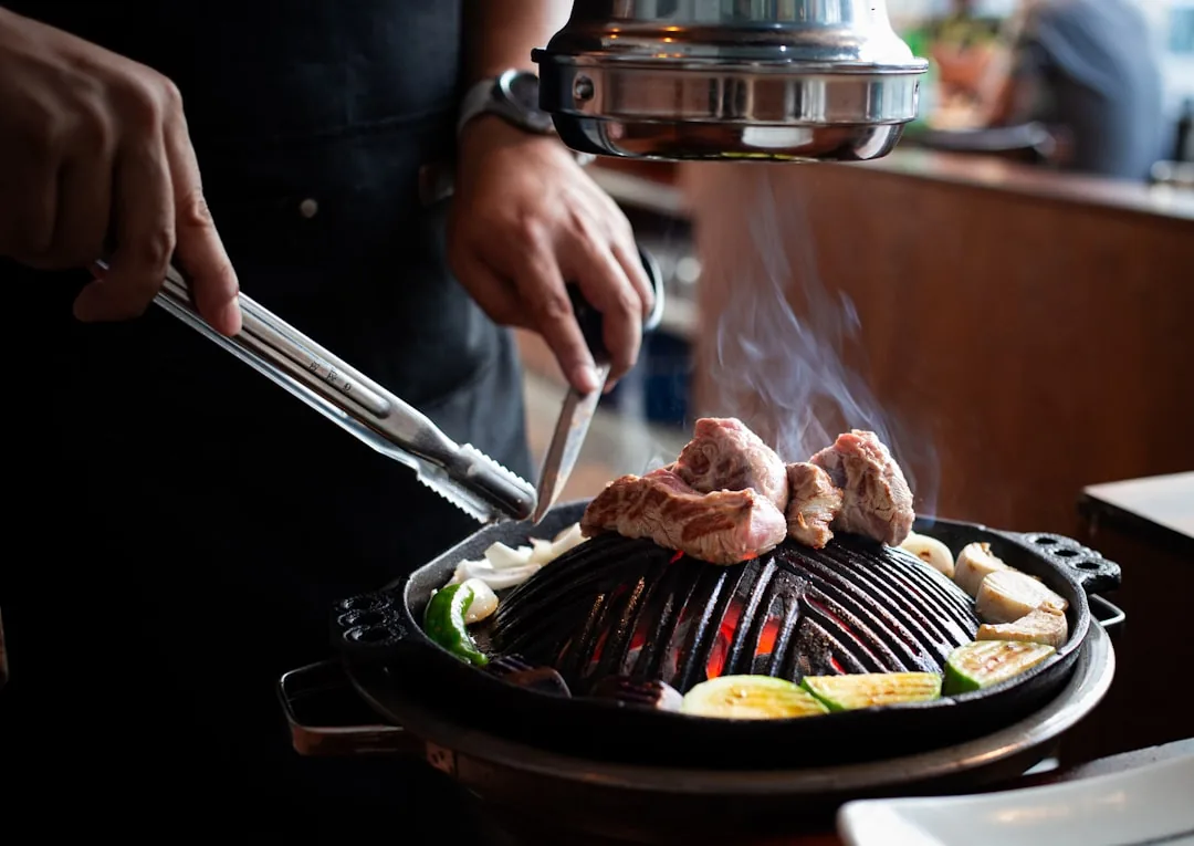 Chef grilling meat and vegetables on a round grill.