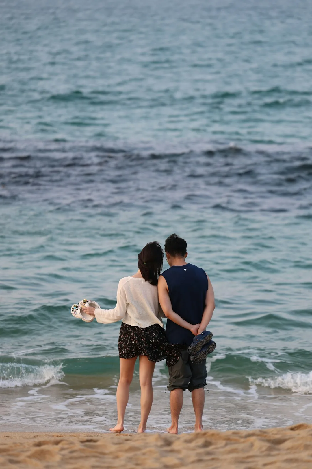 A man and a woman standing on a beach next to the ocean
